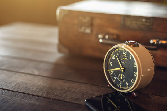 Vintage alarm clock on a wooden rustic table with travel case and strong backlight. Shallow DOF