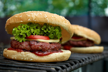 Tasteful white sesame bun burger standing on metal grill surface. Grilled beef on ketchup layer,...