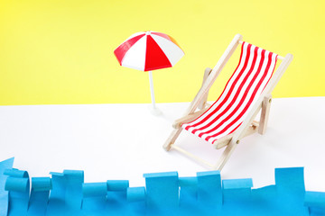 Red deck chair with umbrella near sea. Toy recliner on blue and yellow background. Concept summer rest.