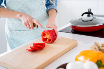 Cropped profile photo of housewife chef arms holding big red pepper bell cutting knife slices enjoy morning cooking tasty dinner family meeting wear apron shirt stand modern kitchen indoors