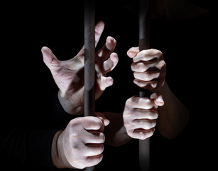 Two people are in prison. Her hands cling to the bars.