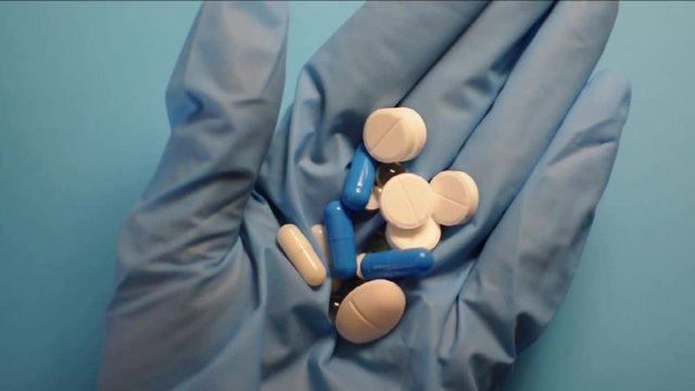 Person holds many pills in blue glove. Medications for taking against COVID19