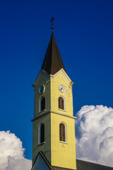 Fototapeta na wymiar Yellow tower of a catholic temple on a background of blue sky and white clouds