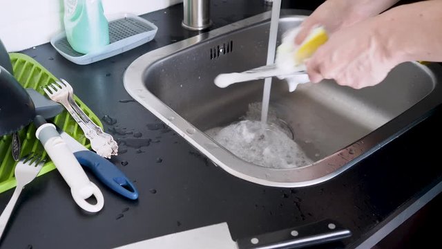 Washing dishes by hand, a young woman without gloves washes knives and other Cutlery in the sink