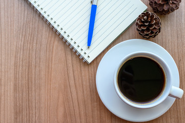 Blank page of note book with black coffee cup, pine cones on wooden table, flat lay