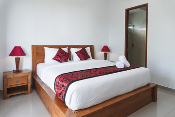 Photograph of bright white bedroom with wooden bed