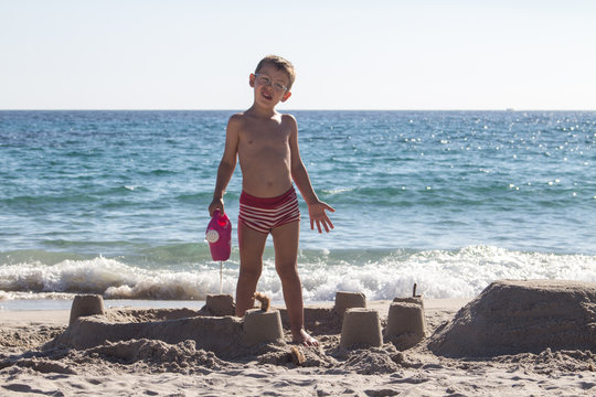 Bambino con occhiali costruisce castello di sabbia