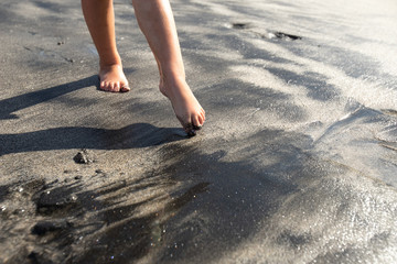 White baby touches the black beach sand in Bali with bare feet