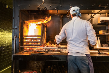 Chef cooking meat and sausages on grill. Focus on meat.