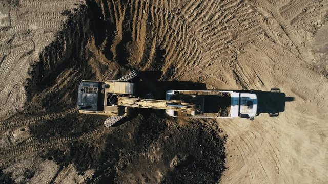 Digger loading earth transportation truck at construction site. Aerial, drone shot.