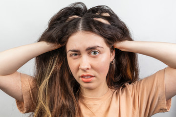The brunette woman nervously scratches her head suffering from itching. White background. The...
