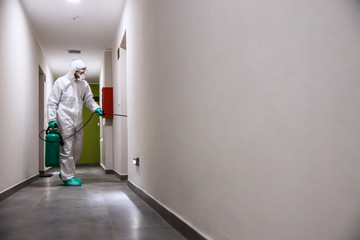 Worker in sterile suit and mask sterilizing hall of a building from corona virus / covid 19.