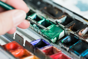 Kunststudent nimmt grüne Aquarellfarbe mit einem kleinen Pinsel auf