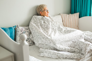 elderly woman sits on a bed in a blanket