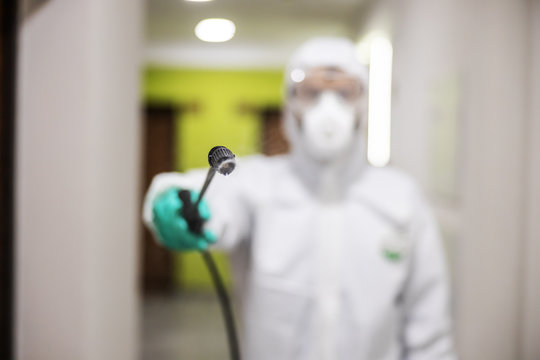 Closeup of worker in protective suit and mask sterilizing building. Selective focus on spray. Protection of corona virus / covid-19 concept. Selective focus on sprayer.