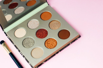 Multi-colored pastel brown red eye shadow on a pink background with brushes.