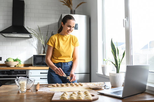 A young woman learns to cook, she watches video recipes on a laptop in the kitchen and cook a dish from the dough. Cooking at home concept