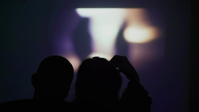 Silhouette of a couple in love on the background of the screen on the wall. A couple is watching a movie on a projector. What to do at home. Watching a movie at home. Stay home. Have fun at home.