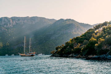 Fototapeta na wymiar Summer concept: A Turkish gulet and behind some luxury white yachts anchored at the Aegean sea with sun beam in background. Natural photo with copy space. Green and blue contrast. No people