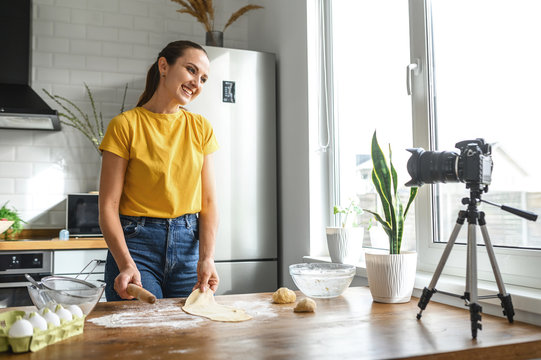 Food vlogs. A young woman makes cooking videos in the kitchen. She uses a rolling pin and dough and looks at the camera with a smile