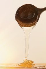 Fresh honey dripping from wooden spoon on yellow background. Thick honey dipping from the wooden ...