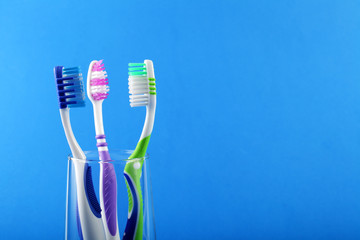 Three toothbrushes in a glass cup on a blue background, place for your text