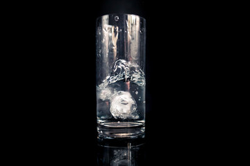 Kostka lodu wpadajaca do szklanki z wodą - obrazy, fototapety, plakaty