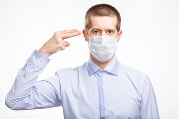A handsome young man in a medical mask, a blue light shirt shows his finger on his head, in full-face, staring at the camera . Isolated