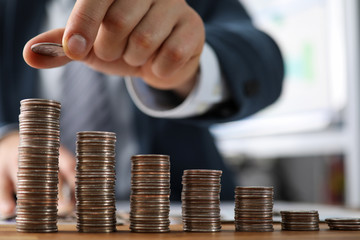 Male hands in suit stack coins on table, saving