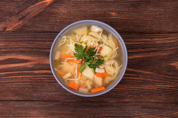 Homemade chicken vegetable soup with noodles on brown wood background, top view and close up