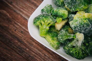 Frozen green cabbage, semi-finished product in a white cup. On a dark wood table. Cooking broccoli...