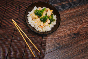 Green cabbage broccoli with rice and white meat. On a dark wooden table. Asian traditional dish. Chinese chopsticks