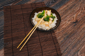 Green cabbage broccoli with rice and white meat. On a dark wooden table. Asian traditional dish. Chinese chopsticks