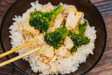 Green cabbage broccoli with rice and white meat. On a dark wooden table. Asian traditional dish. Chinese chopsticks
