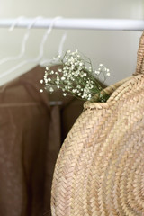 Straw bags with gypsophila flowers and neutral color wardrobe on a clothing rack. Selective focus.