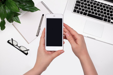 Top view of woman hands holding smartphone with blank screen at workplace