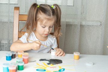 beautiful girl 3-4 years old dips a brush in a jar of white paint. children's creativity during the period of self-isolation and quarantine in connection with the coronavirus. focus on the baby's hand