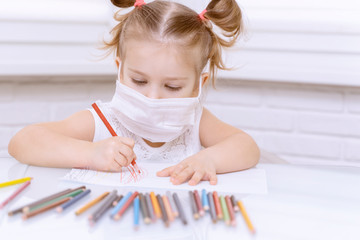 little girl in a disposable mask draws with crayons at the table.