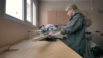 Girl in a workshop sawing wooden materials
