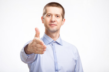 successful friendly man pulls his hand to say hello, for a snooto, in a blue light casual shirt staring at the camera. Isolated