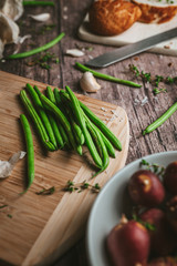 
Close-up of green prepared fine beans on a rustic table with red potatoes with garlic and rosemary Vertical