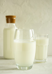 Milk in a transparent glass on a light gray background on the background of a bottle with milk and a glass with milk