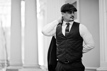 Portrait of retro 1920s english arabian business man wearing dark suit, tie and flat cap.