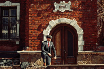 Portrait of retro 1920s english arabian business man wearing dark suit, tie and flat cap standing...