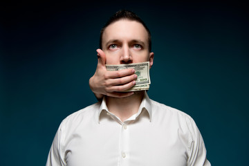 Buying silence for dollars. mouth of a man in white shirt is covered with money