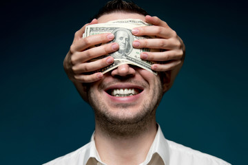 A man blinded by money. Hands out of darkness close man s eyes with dollar bills