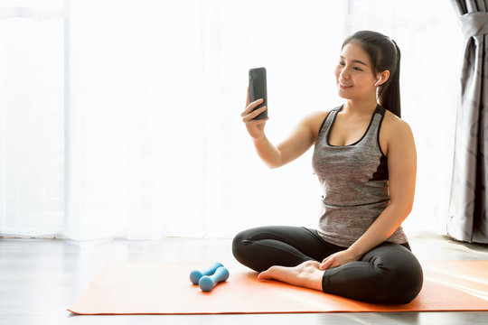 Smiley Asian woman wearing sportswear sitting orange mat and take a photo of yourself while exercising.