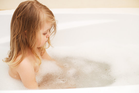 Funny little baby girl with blond hair playing with foam in a bath tub. girl takes a bath