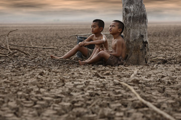 The boy sat on the arid ground, waiting for rain. Due to global warming Global warming and climate change concepts - obrazy, fototapety, plakaty
