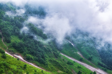 The green slopes of high mountains are hidden in clouds and fog. Melting snow in high mountains in...